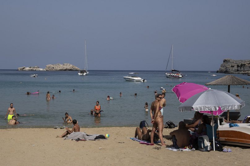 Tourists enjoy the beach and the sea in Lindos, on the Aegean Sea island of Rhodes, southeastern Greece.