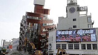Un banner con su scritto "Mai arrendersi. Forza Hualien" accanto a un edificio inclinato dal terremoto del 3 aprile, Hualien City, Taiwan, 4 aprile 2024