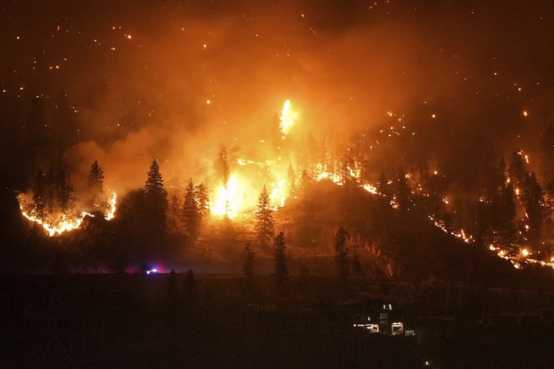 O incêndio florestal de McDougall Creek arde na encosta de uma montanha acima de uma casa à beira do lago em West Kelowna, Canadá.