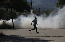 A man runs for cover as riot police launch tear gas in an effort to remove street vendors in Port-au-Prince, Haiti, Tuesday, April 2, 2024.