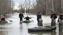 Police officers stand guarding an area as people use rubber boats in a flooded street after part of a dam burst, in Orsk, Russia. 