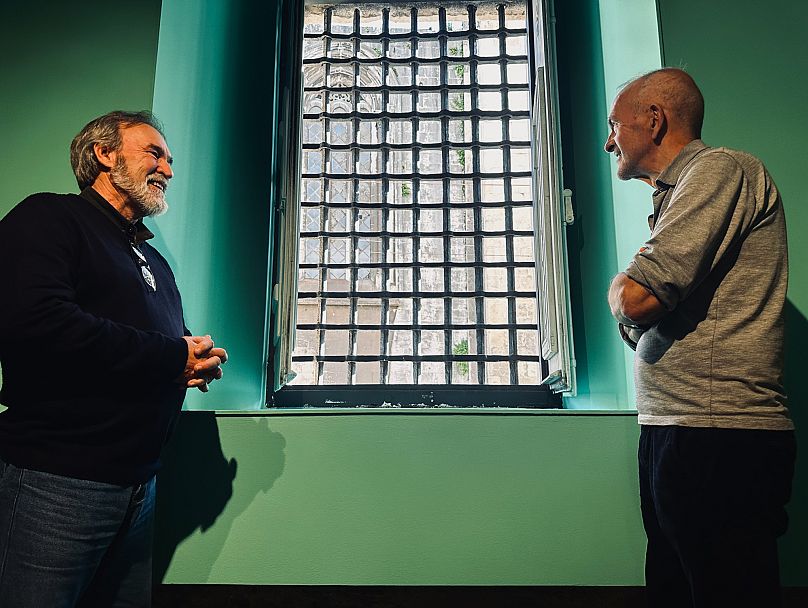 Arnaldo Silva e José Martins olham pela janela do Museu do Aljube, antiga prisão e atual museu da resistência.