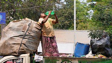 Уборщица мусора утоляет жажду, стоя на грузовике в жаркий день в Хайдарабаде, Индия, 12 марта 2024 года.