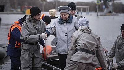 Emergency workers assist a woman to deboard a boat during evacuations local residents in a flooded street after a part of a dam burst, in Orsk, Russia on Monday, April 8, 2024