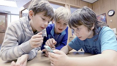 Three children look at a smartphone