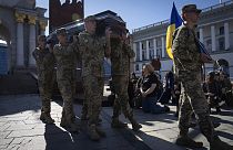 People kneel as soldiers carry the coffins of Ukrainian servicemen during the funeral ceremony in Independence square in Kyiv, Ukraine, Tuesday, April 9, 2024.