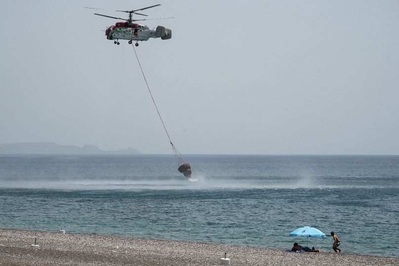 Beachgoers watch a helicopter filling water from the sea during a wildfire, near Gennadi village, on the Aegean Sea island of Rhodes last July
