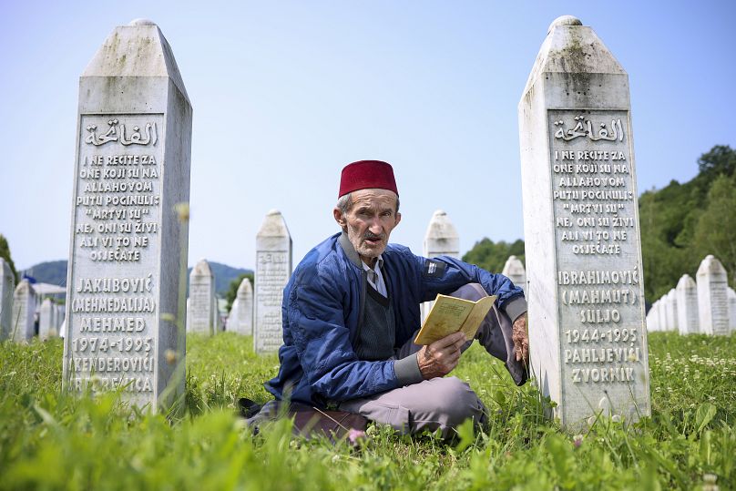 A Bosnian muslim man prays next to the grave of his relative, victim of the Srebrenica genocide