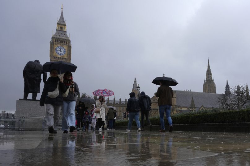 Tourists hold umbrellas against the rain as they walk in Parliament Square.