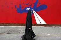 A woman walks past a new anti-U.S. mural on the wall of former US embassy in Tehran, 2019. 