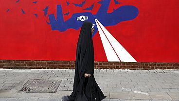 A woman walks past a new anti-U.S. mural on the wall of former US embassy in Tehran, 2019. 