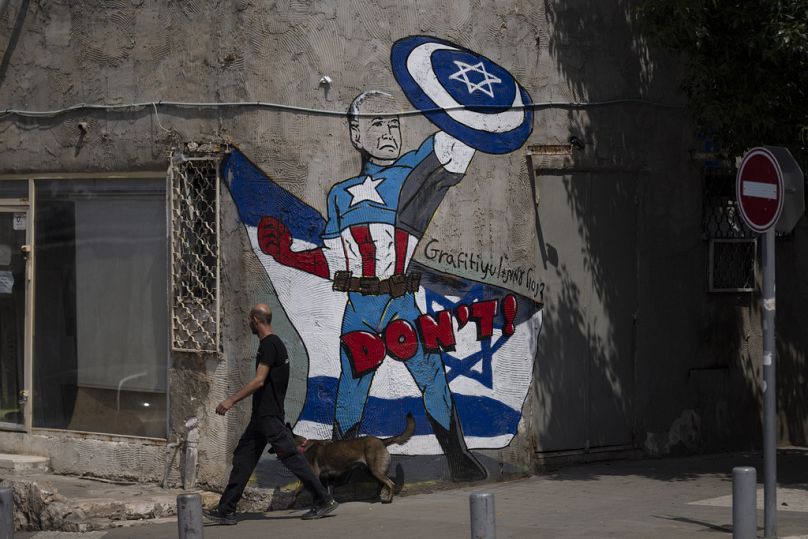 A man walks past a mural depicting the US President Joe Biden as a superhero defending Israel on a street in Tel Aviv, April 2024