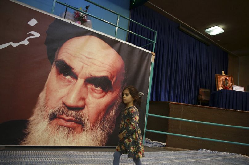 In this Tuesday, Jan. 22, 2019, photo, a girl walks past a poster of Ayatollah Ruhollah Khomeini,.