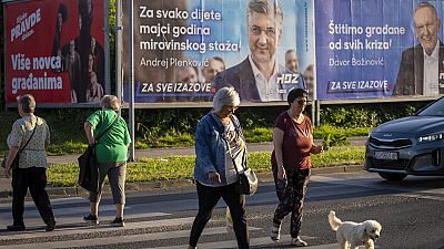 Pedoni davanti ai manifesti elettorali del Partito socialdemocratico a Zagabria, in Croazia, 14 aprile 2024