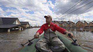 Ein Mann rudert durch ein überflutetes Dorf.