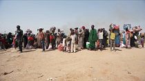 Ampia inquadratura di rifugiati sudanesi in piedi vicino a un rifugio