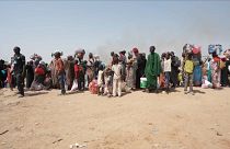 Ampia inquadratura di rifugiati sudanesi in piedi vicino a un rifugio