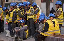 Workers wait for transport outside a construction site in Beijing, Tuesday, April 9, 2024. 