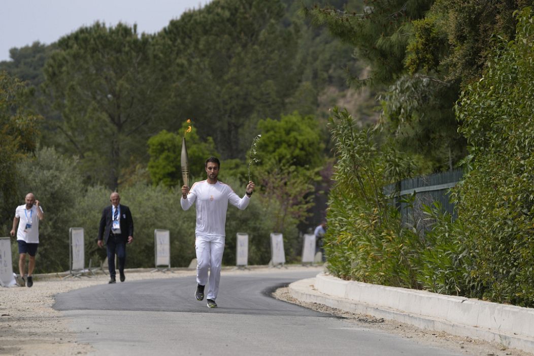 The first torch bearer, Greek olympic gold medalist Stefanos Douskos, runs towards the monument to Pierre de Coubertin.
