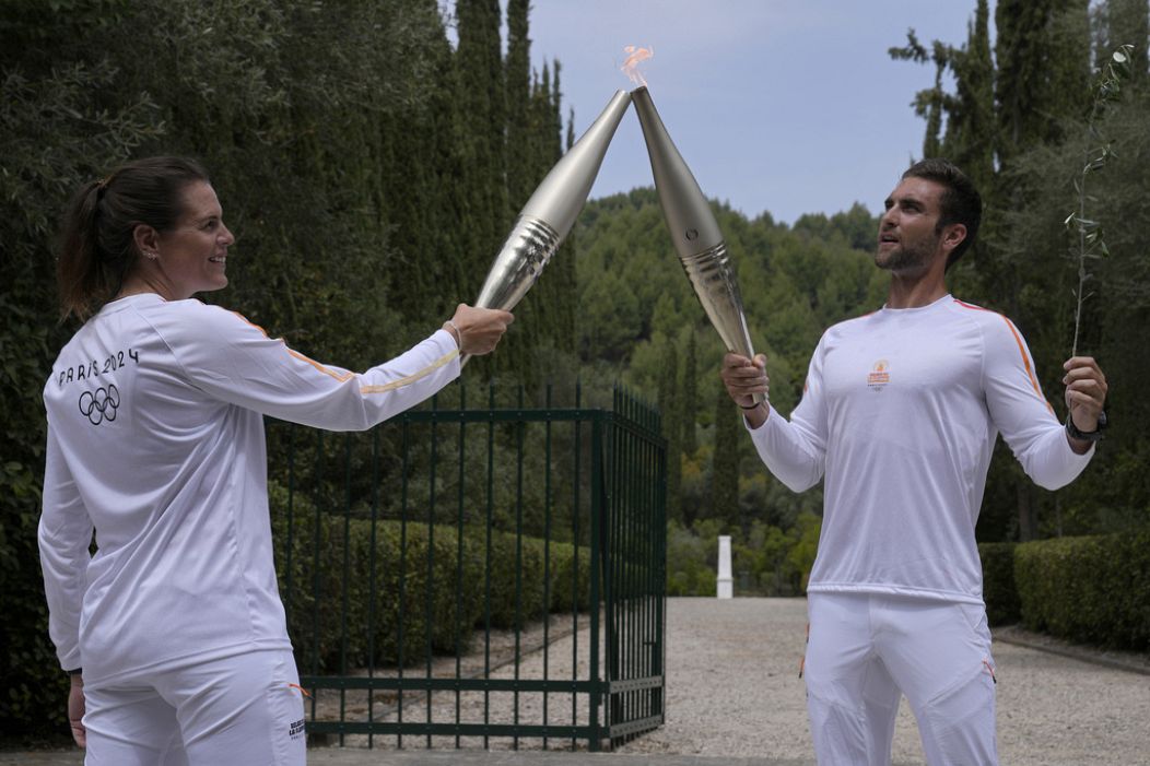 The first torch bearer, Greek olympic gold medalist Stefanos Douskos, right, passes the flame to first French torchbearer, three-time Olympic medallist Laure Manaudou.