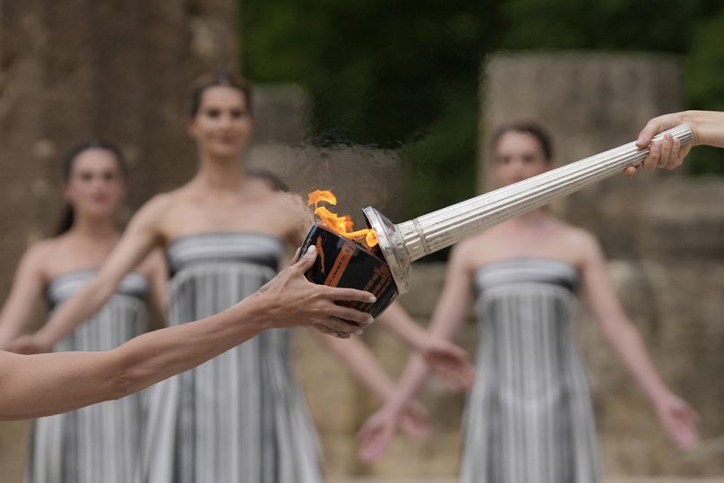 ctress Mary Mina, playing high priestess, right, lights a torch during the official ceremony of the flame lighting for the Paris Olympics