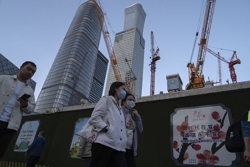 Women wearing masks pass by construction cranes near the central business district in Beijing, Tuesday, April 16, 2024