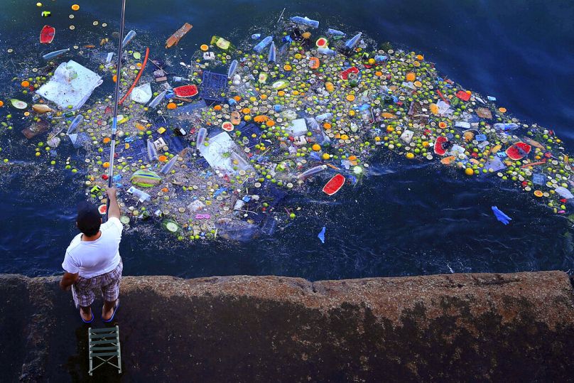 A man holds a fishing rod as floating trash hits the coastline of the Mediterranean Sea in Beirut, September 2016