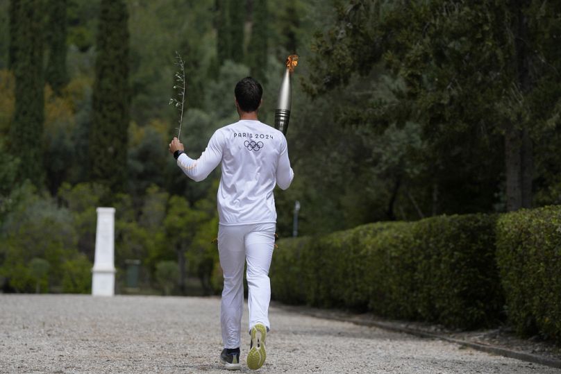 The first torch bearer, Greek olympic gold medalist Stefanos Douskos, runs towards the monument to Pierre de Coubertin.