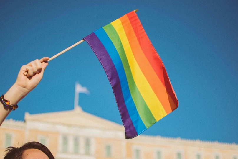 An LBGTQ+ ally flies a rainbow flag in Syntagma Square in Athens, Greece