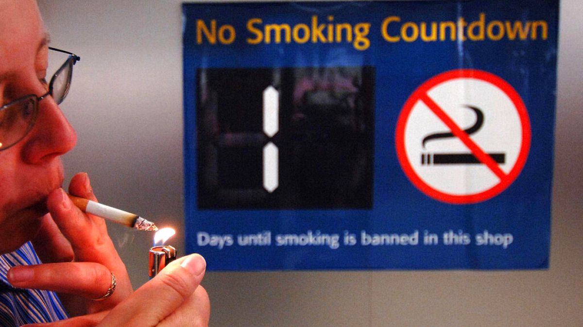 Sigara yasağı için geri sayımın başladığını bildiren  tabela önünde sigara yakan bir kişi