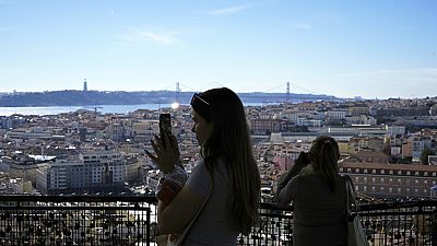 Turistas tiram fotografias do miradouro de Nossa Senhora do Monte, com vista para o rio Tejo e para a baixa de Lisboa, num dia de sol quente.