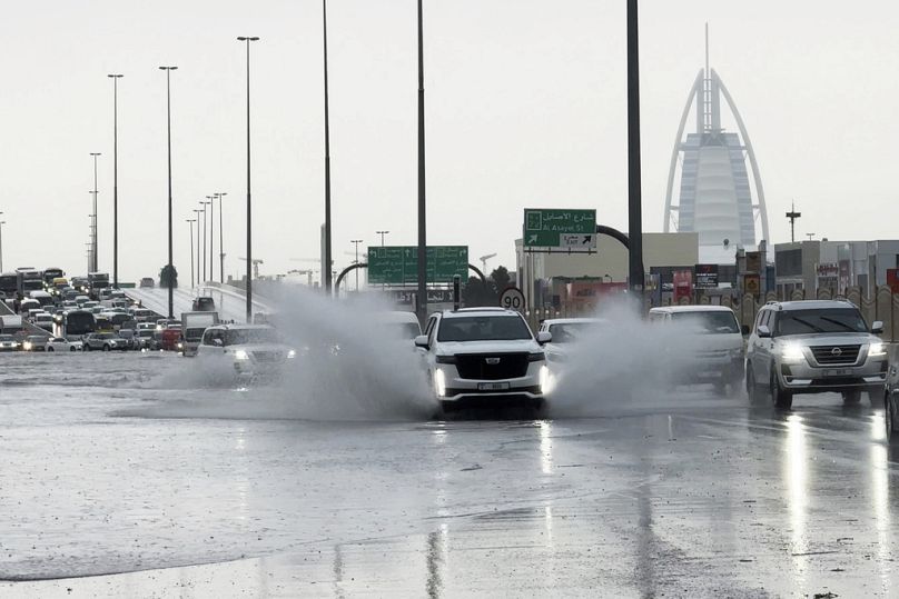 An SUV splashes through standing water on a road in Dubai, with the Burj Al Arab luxury hotel in the background. in Dubai