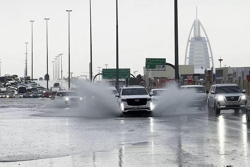 Ein Geländewagen fährt durch stehendes Wasser auf einer Straße, im Hintergrund ist das Luxushotel Burj Al Arab in Dubai, Vereinigte Arabische Emirate, zu sehen.