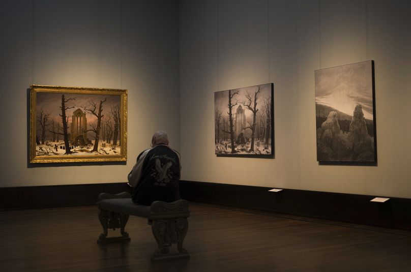 A man sits in front of a copy of Caspa David Friedrich's painting Monastery Cemetery In Snow' at the Alte Nationalgalerie museum in Berlin, Germany.