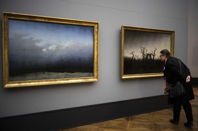 A woman inspects Caspar David Friedrich's painting 'Abby Among The Oaks' whis is displayed next to 'Monk By The Sea' during a press preview.