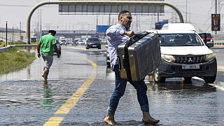 A man carries luggage through floodwater caused by heavy rain while waiting for transportation in Dubai, United Arab Emirates on Thursday