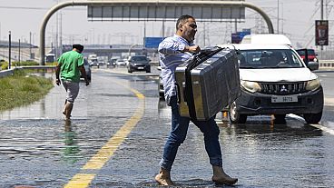 A man carries luggage through floodwater caused by heavy rain while waiting for transportation in Dubai, United Arab Emirates on Thursday