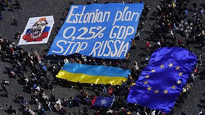 المتجمعون يرفعون لافتة تطالب بتخصيص 0.25% من الناتج القومي لكل دولة لدعم أوكرانيا