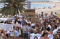 Varias personas desfilan junto a una playa durante una manifestación contra el turismo excesivo que afecta a la población local con viviendas inaccesibles, en las Islas Canarias.