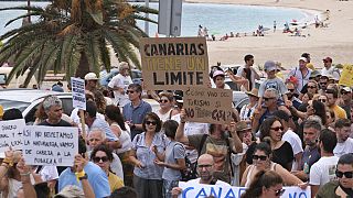 Άνθρωποι περνούν από μια παραλία κατά τη διάρκεια μιας διαδήλωσης κατά του υπερτουρισμού που πλήττει τον τοπικό πληθυσμό με δυσπρόσιτες κατοικίες, στα Κανάρια Νησιά.