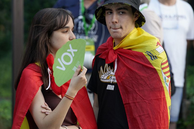 Supporters of far-right Vox party wearing Spanish flags over their shoulders stand outside the party headquarters in Madrid.