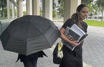 La famosa diseñadora de bolsos Nancy González se esconde bajo un paraguas mientras camina con su abogada Andrea López fuera de la corte federal el lunes 22 de abril de 2024, en Miami.