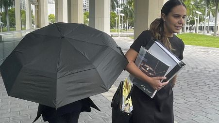 Celebrity handbag designer Nancy Gonzalez hides under an umbrella as she walks with her lawyer Andrea Lopez outside the federal courthouse Monday, April 22, 2024, in Miami.