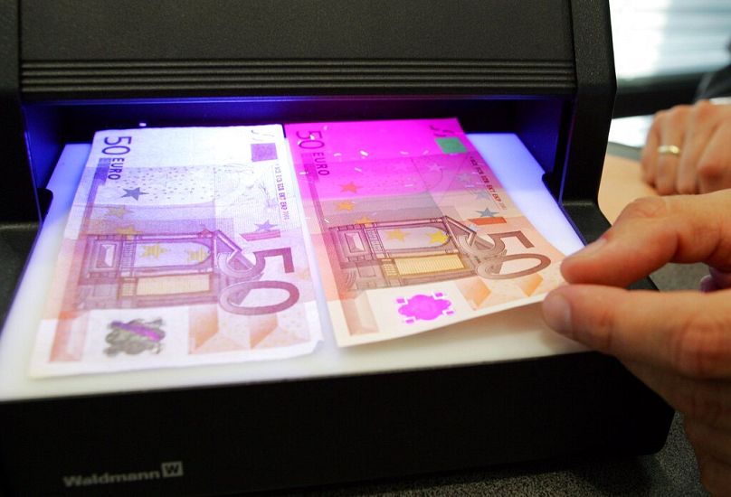 An employee of the Bundesbank checks a fake (left) and a real 50 euro note under a UV light device, October 2005
