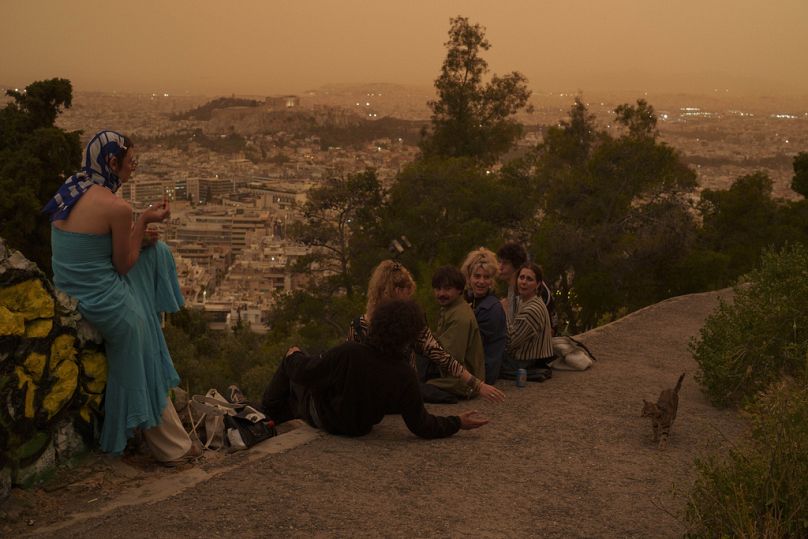Tourists play with a cat at Lycabettus hill as the city of Athens with the ancient Acropolis hill is seen at the background, on Tuesday, April 23, 2024.
