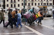 Un portiere trasporta i bagagli dei turisti fuori dalla stazione ferroviaria principale di Venezia, Italia, mercoledì 24 aprile 2024