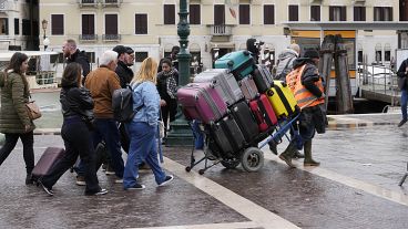 Un portiere trasporta i bagagli dei turisti fuori dalla stazione ferroviaria principale di Venezia, Italia, mercoledì 24 aprile 2024