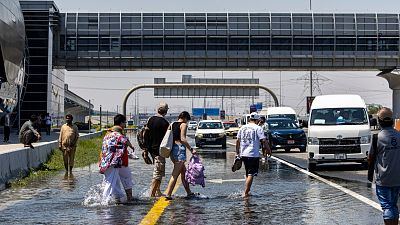 People walk through floodwater caused by heavy rain while waiting for transportation on Sheikh Zayed Road highway in Dubai.