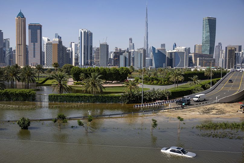 An abandoned vehicle stands in floodwater caused by heavy rain with the Burj Khalifa, the world's tallest building, seen in the background.