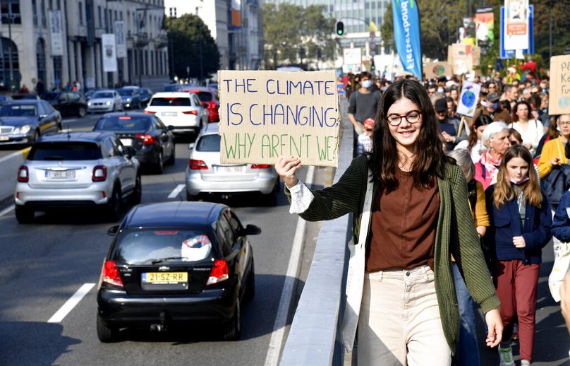 A girl holds up a sign to oncoming traffic as she participates in a climate march and demonstration in Brussels, October 2021